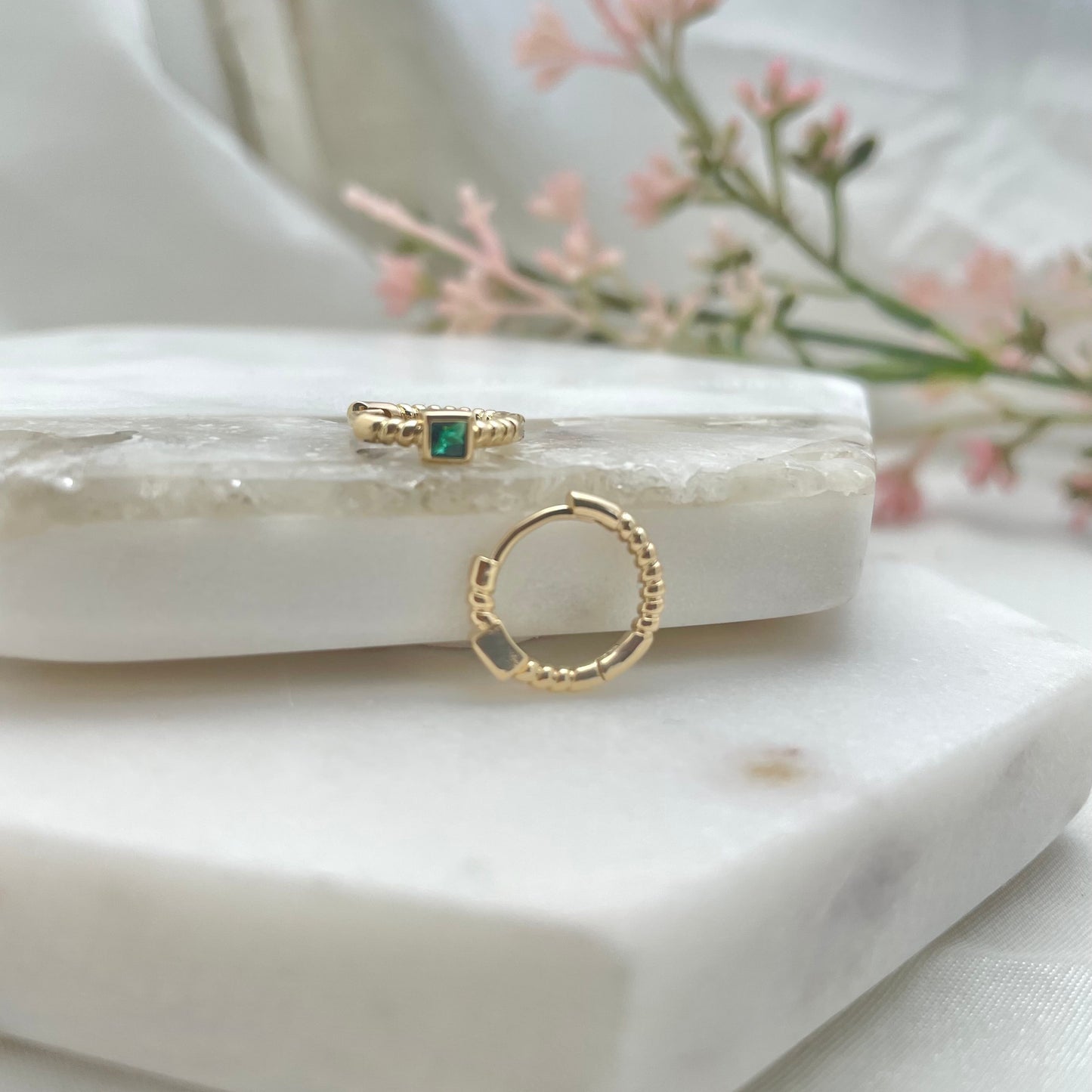front and side view of a pair of huggie hoop earrings with green crystal