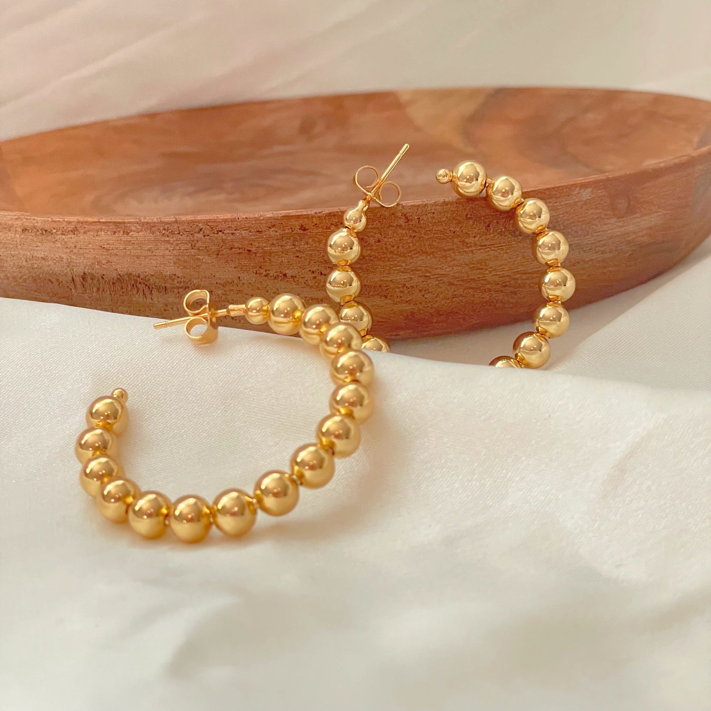 Large beaded hoop earrings over white silk fabric and wooden tray