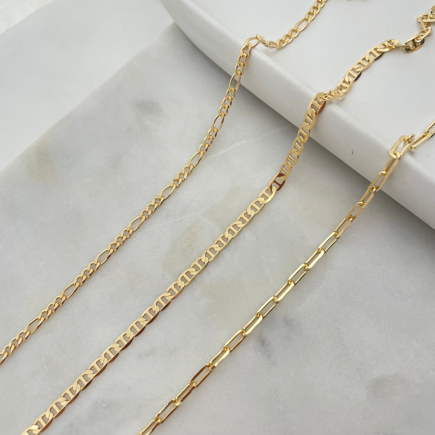 Close up of a 3mm gold filled set of anklets, paperclip, figaro and flat marine.