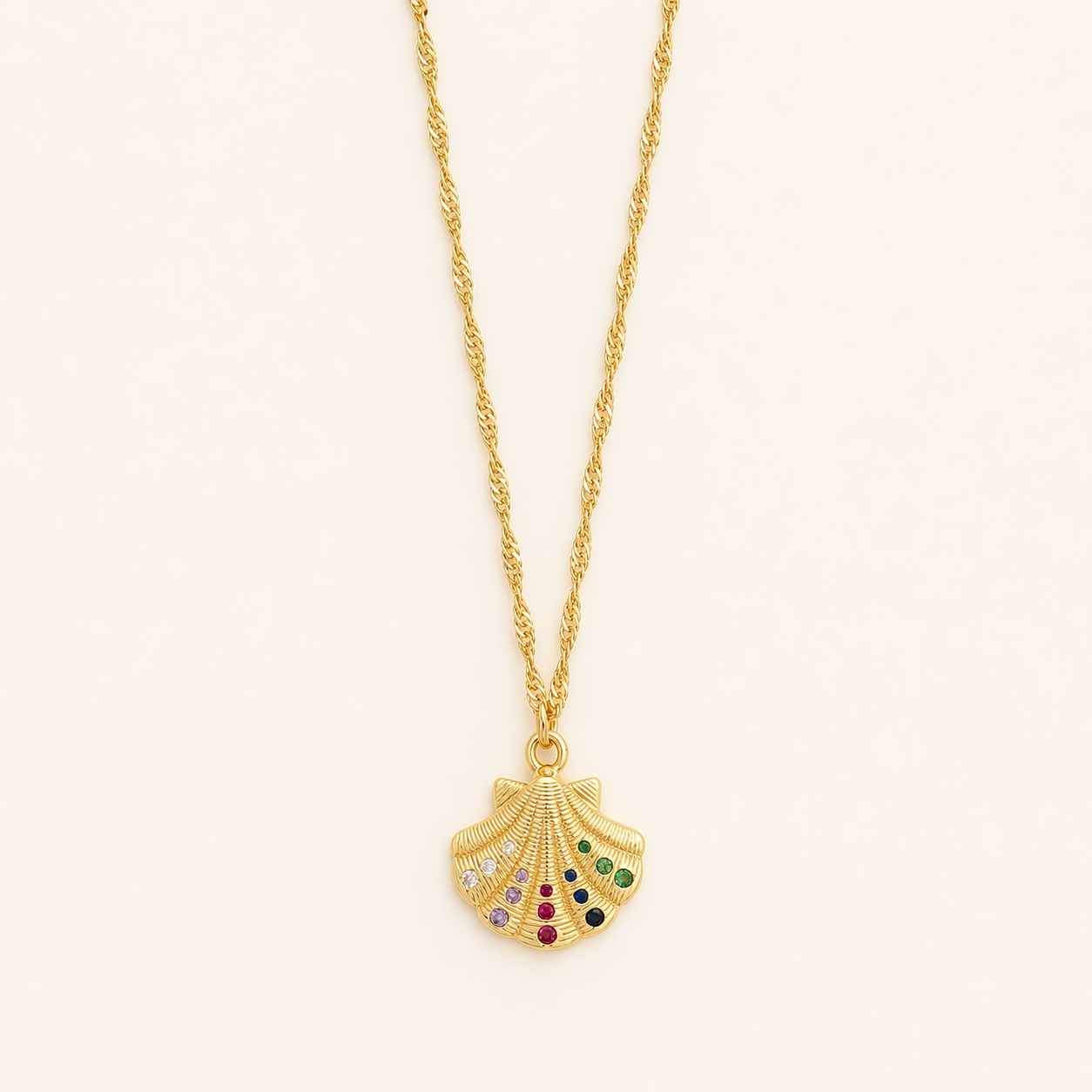 Gold necklace with a shell pendant featuring colorful stones on a beige background