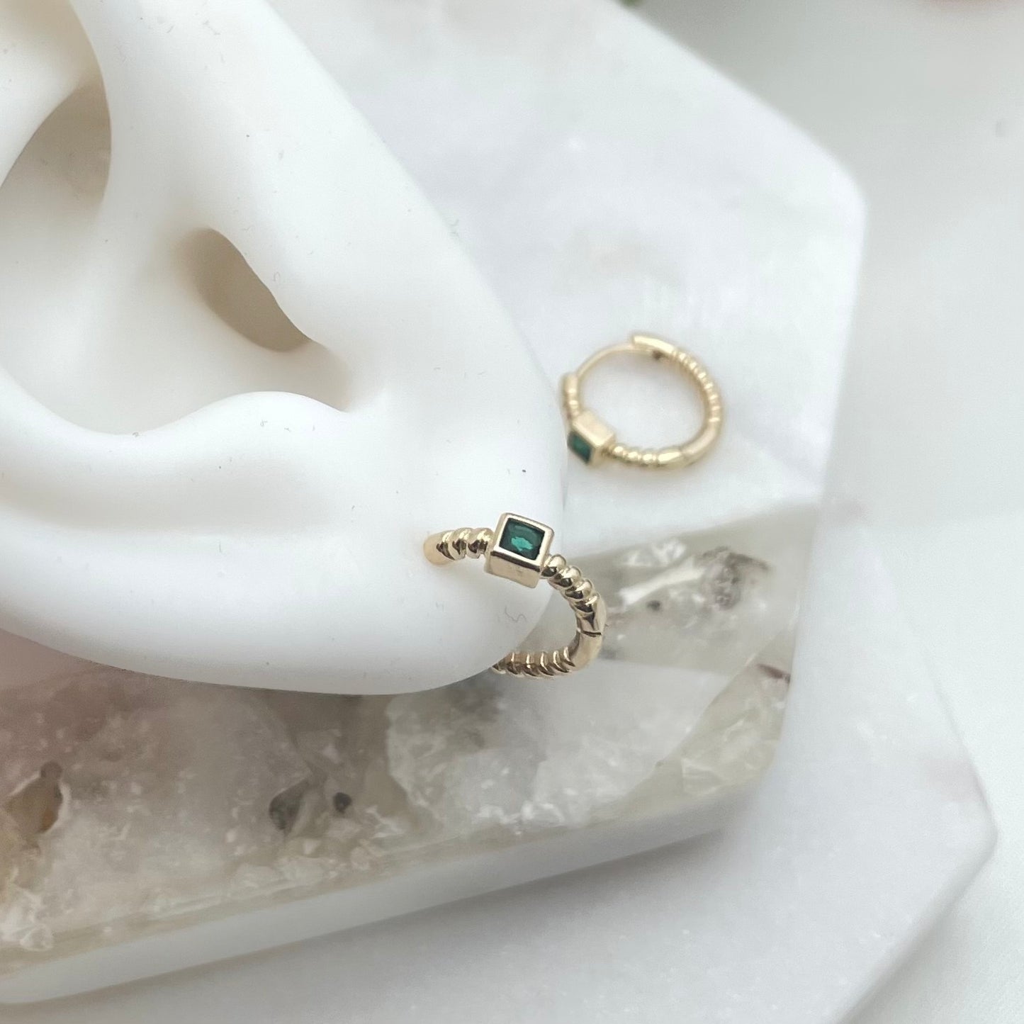 Upper lool of huggie hoop earring with green crystal on a silicone ear