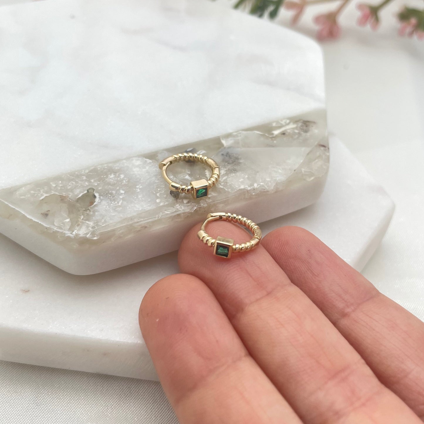 Close up to dainty hoop earring in gold filled with emerald like crystal