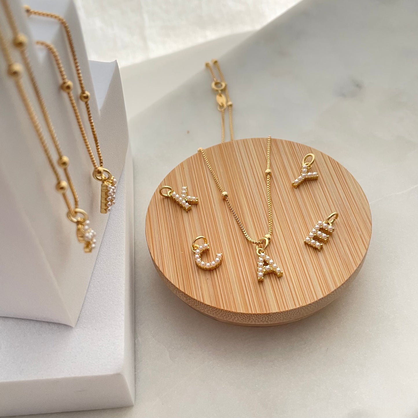 Close up to multiple letter necklaces over a wooden tray and white background