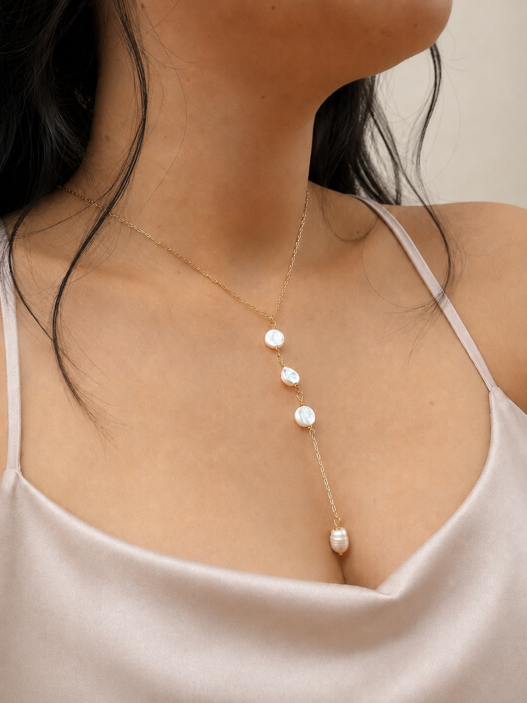 A close-up of a model wearing a delicate gold Y-necklace with four white baroque pearls, styled with a light beige satin camisole.