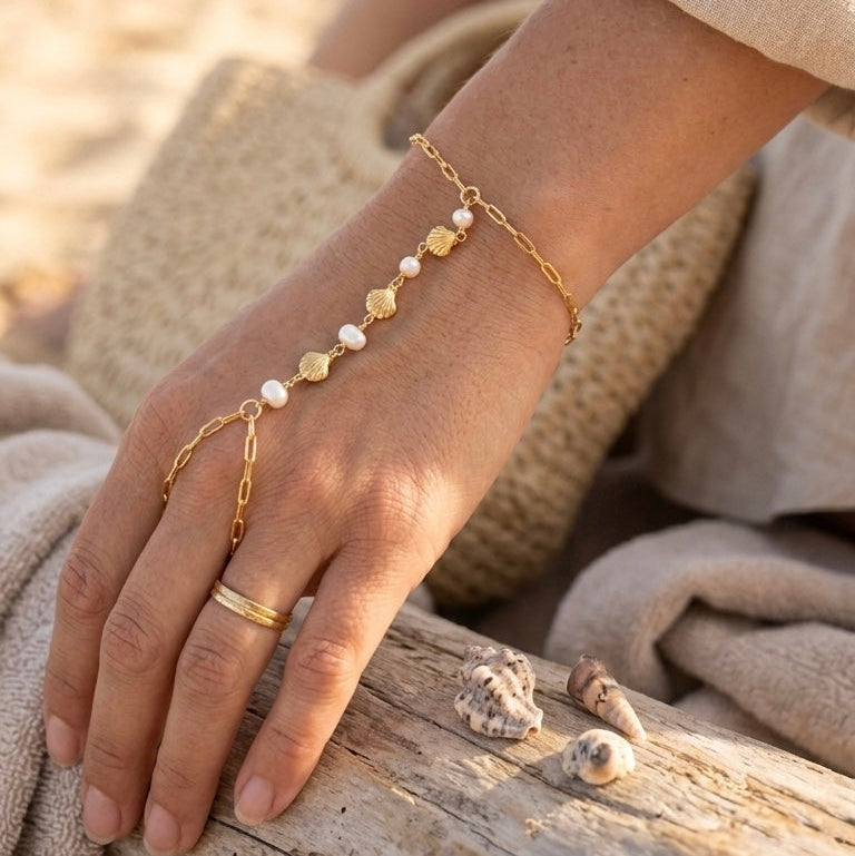 Person wearing gold bracelets with pearls on a beach