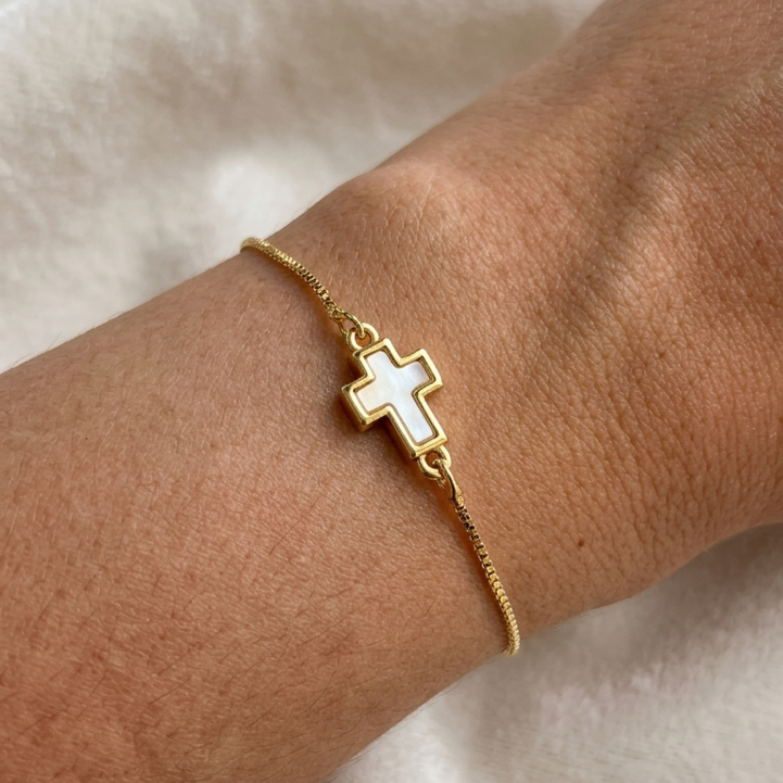 Gold bracelet with a cross charm on a person's wrist against a light background