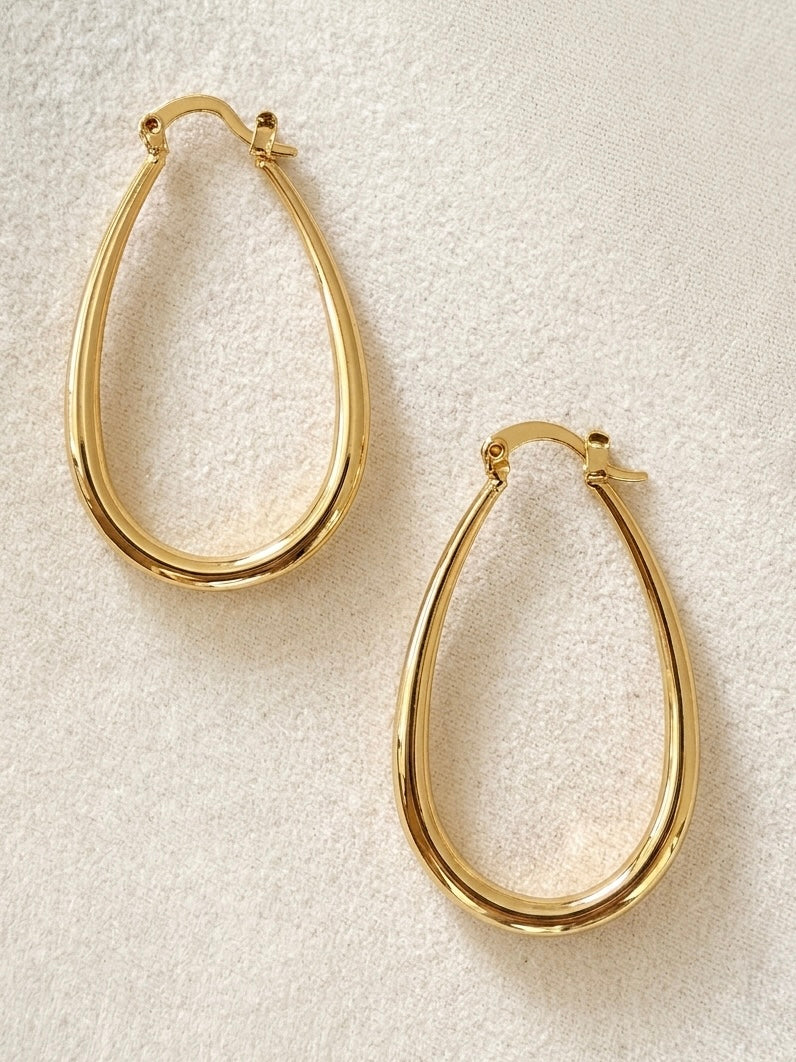 A pair of polished gold filled teardrop hoop earrings with a latch clasp, displayed on a textured off-white fabric background.