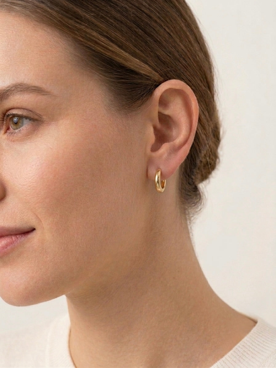 A close-up side profile of a woman wearing a 16mm gold filled hoop earring on her earlobe against a clean off-white background.