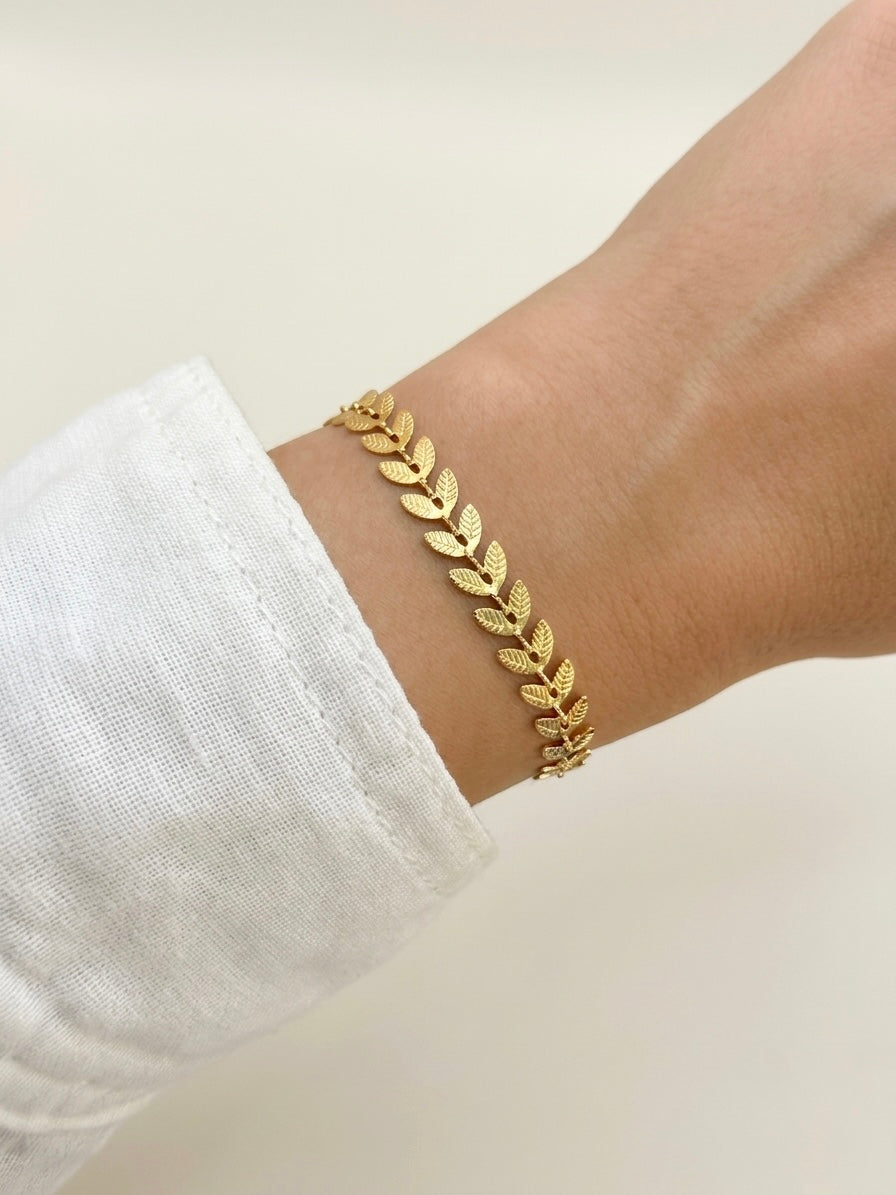 A delicate gold filled leaf bracelet worn on a person's wrist, styled with a white linen sleeve against a soft, light beige background.