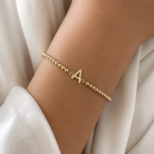 Gold bracelet with a letter 'A' on a wrist against a white fabric background