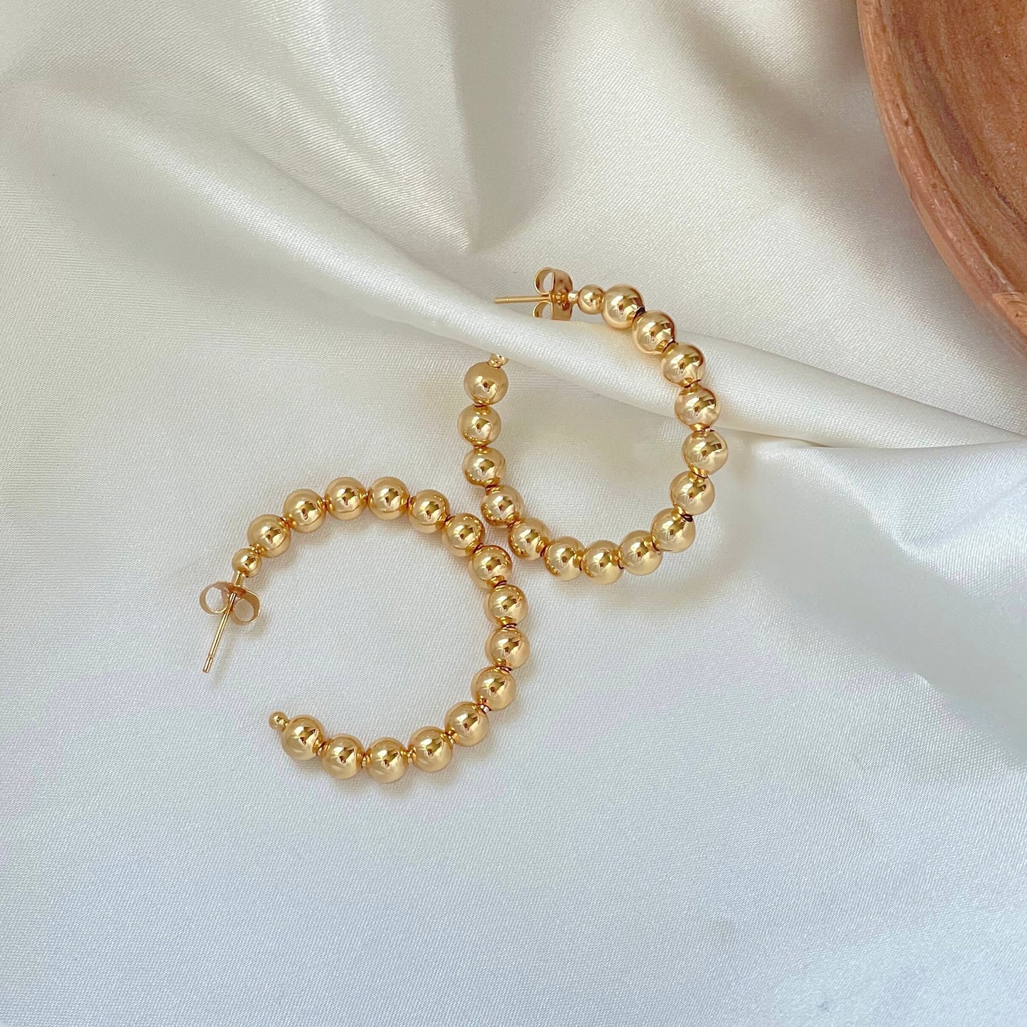 Close look to beaded hoop earrings with polished sphere design displayed on neutral fabric on background