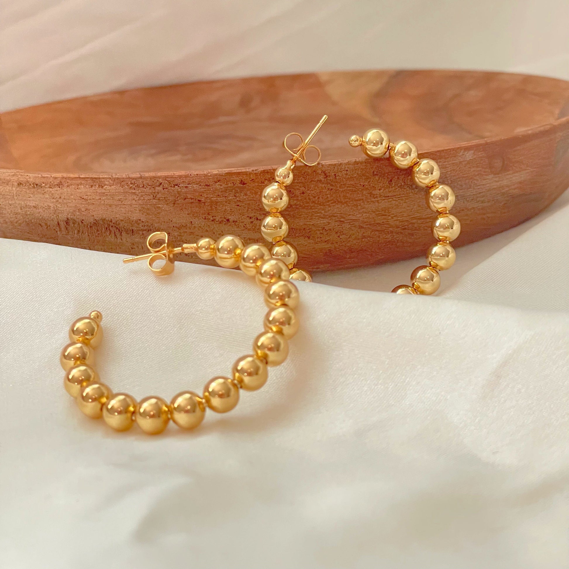 Large beaded hoop earrings over white silk fabric and wooden tray
