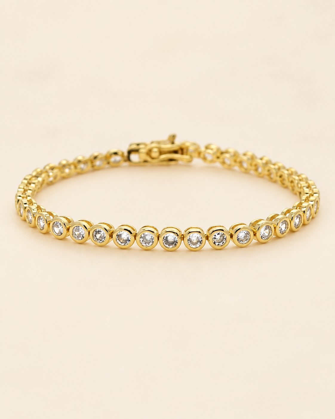Gold-tone bezel tennis bracelet with round clear stones on a soft cream background.