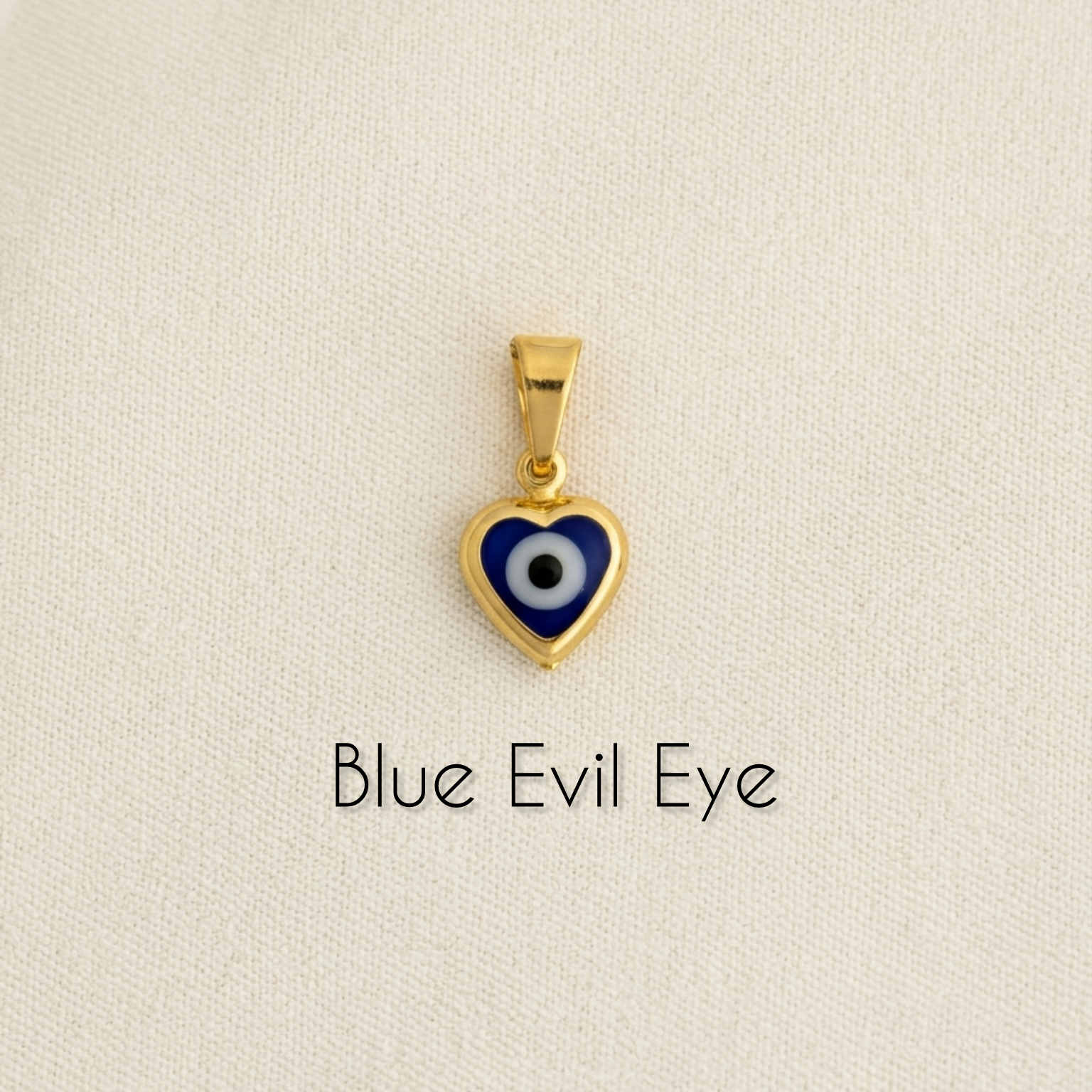 Gold filled heart-shaped blue evil eye pendant on a beige background