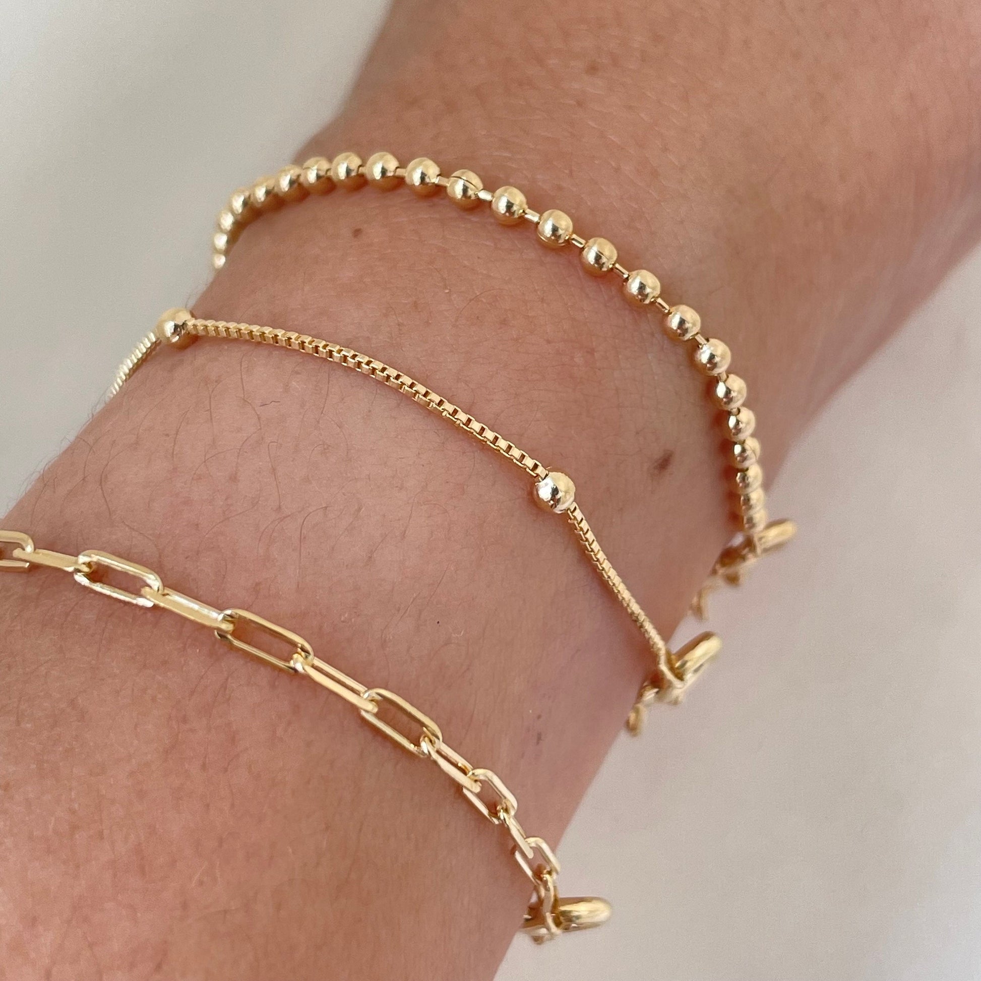 Bracelets on wrist, paperclip, satellite and beaded bracelet all in 18k gold filled