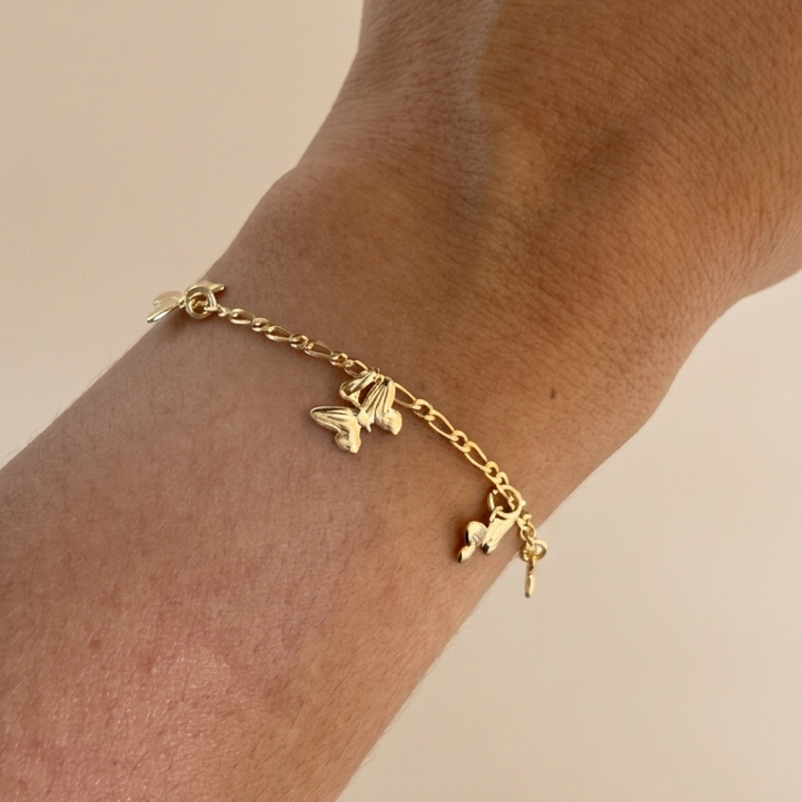 Close up Gold filled bracelet with butterfly charms on a wrist against a beige background