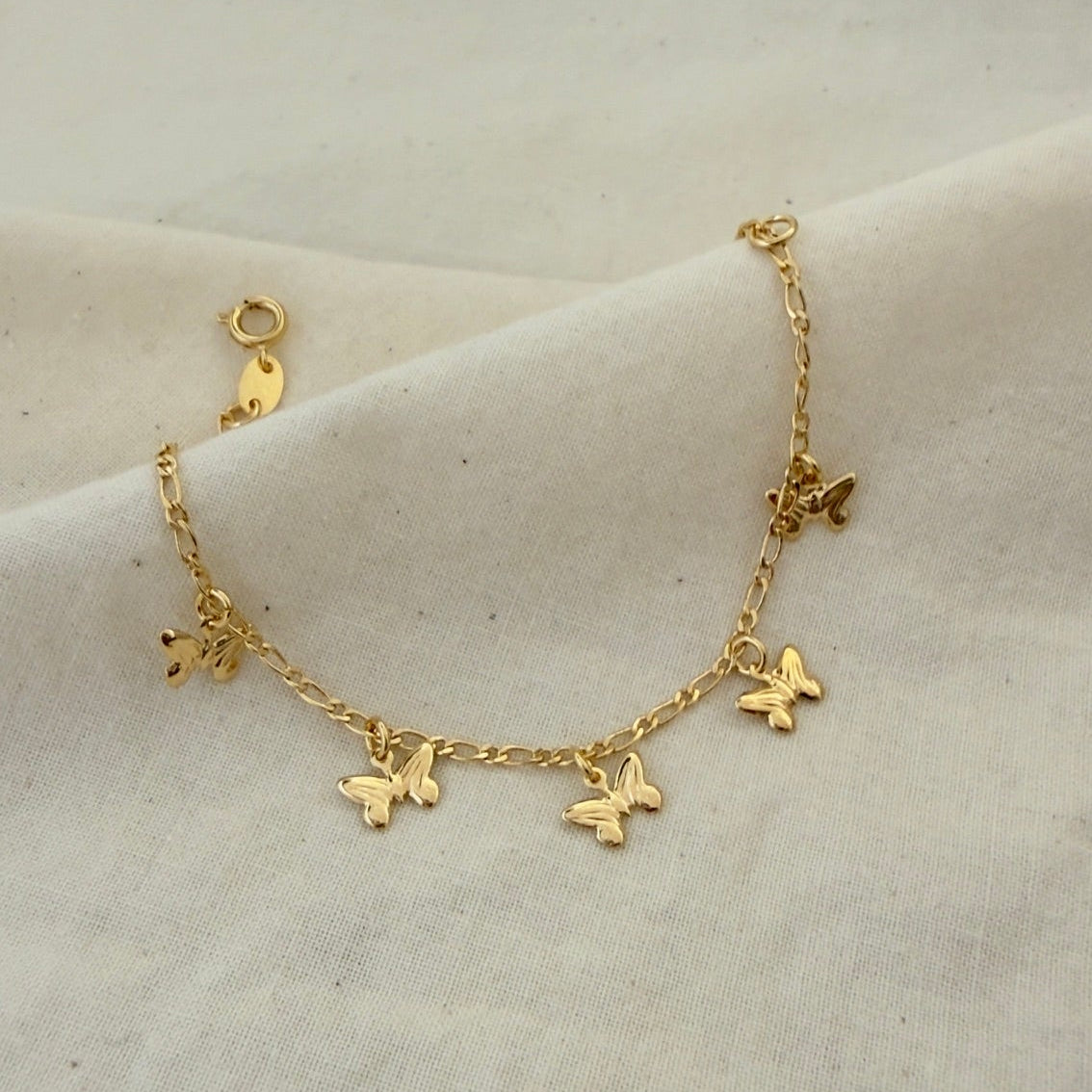 Gold bracelet with butterfly charms on a beige fabric background