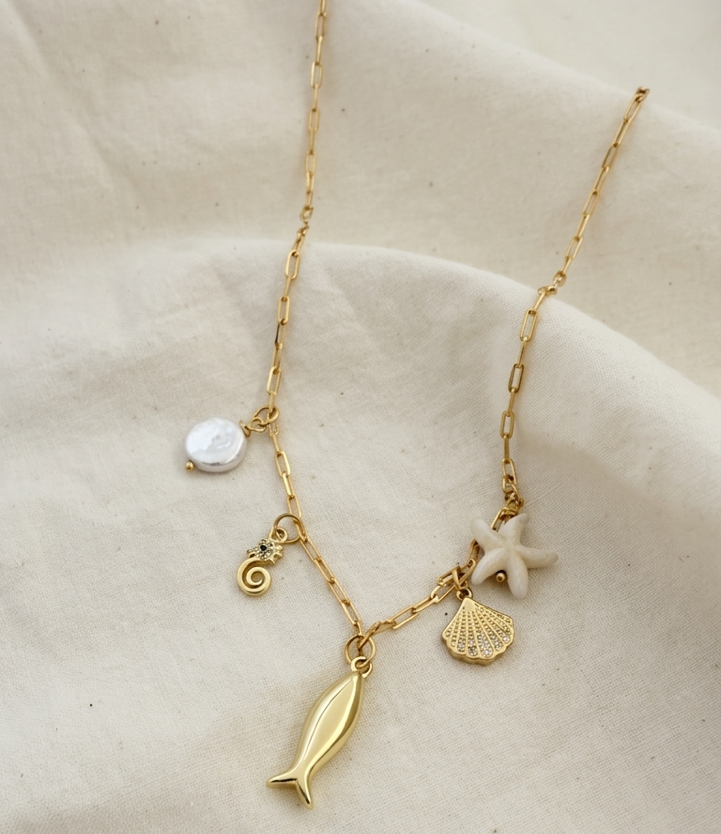 Gold filled necklace with 5 charms, seahorse, fish, shell, starfish and pearl over linen background