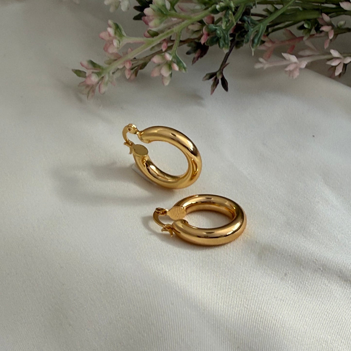 Gold hoop earrings on a white fabric background with flowers and  greens background