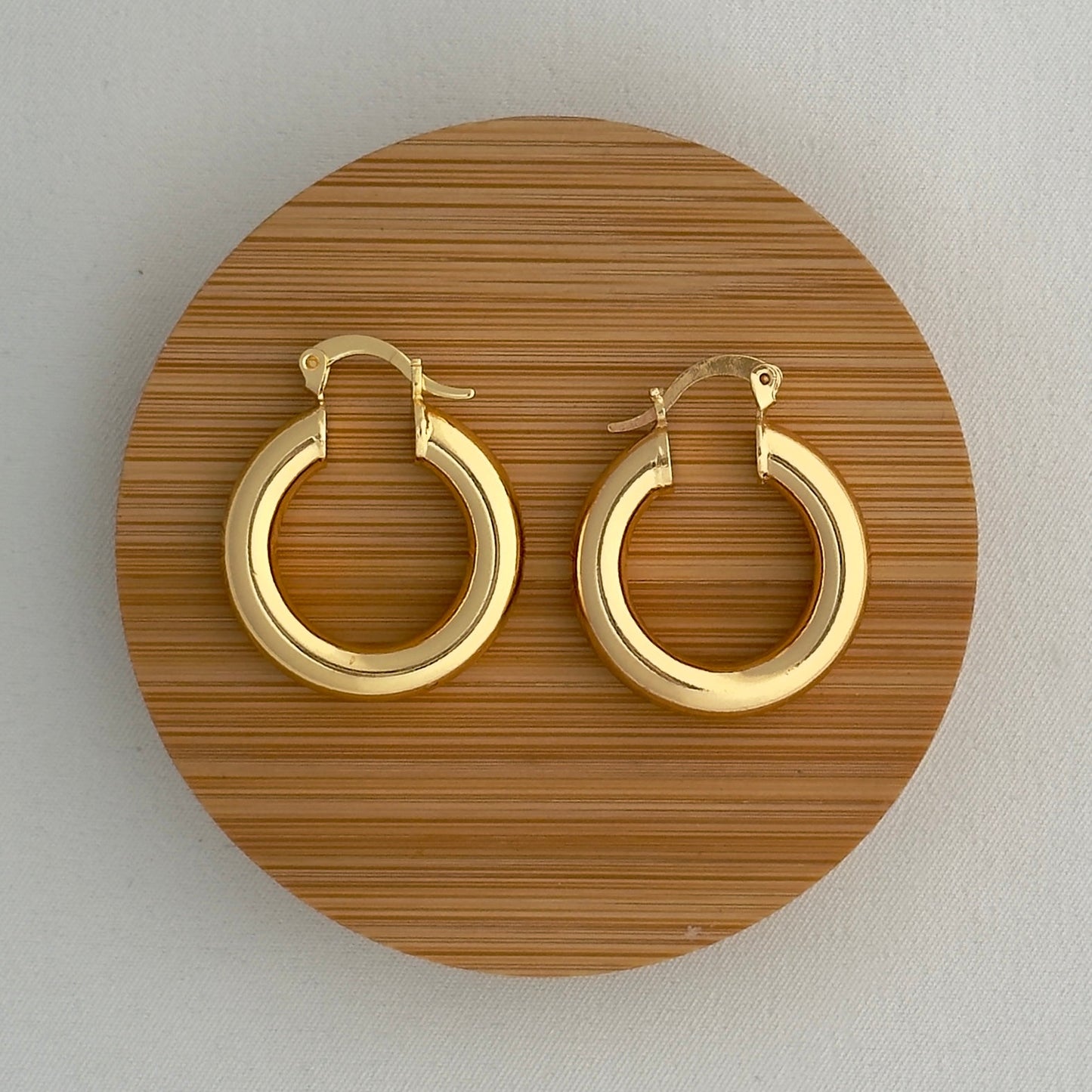 Gold hoop earrings on a wooden circular stand against a light background