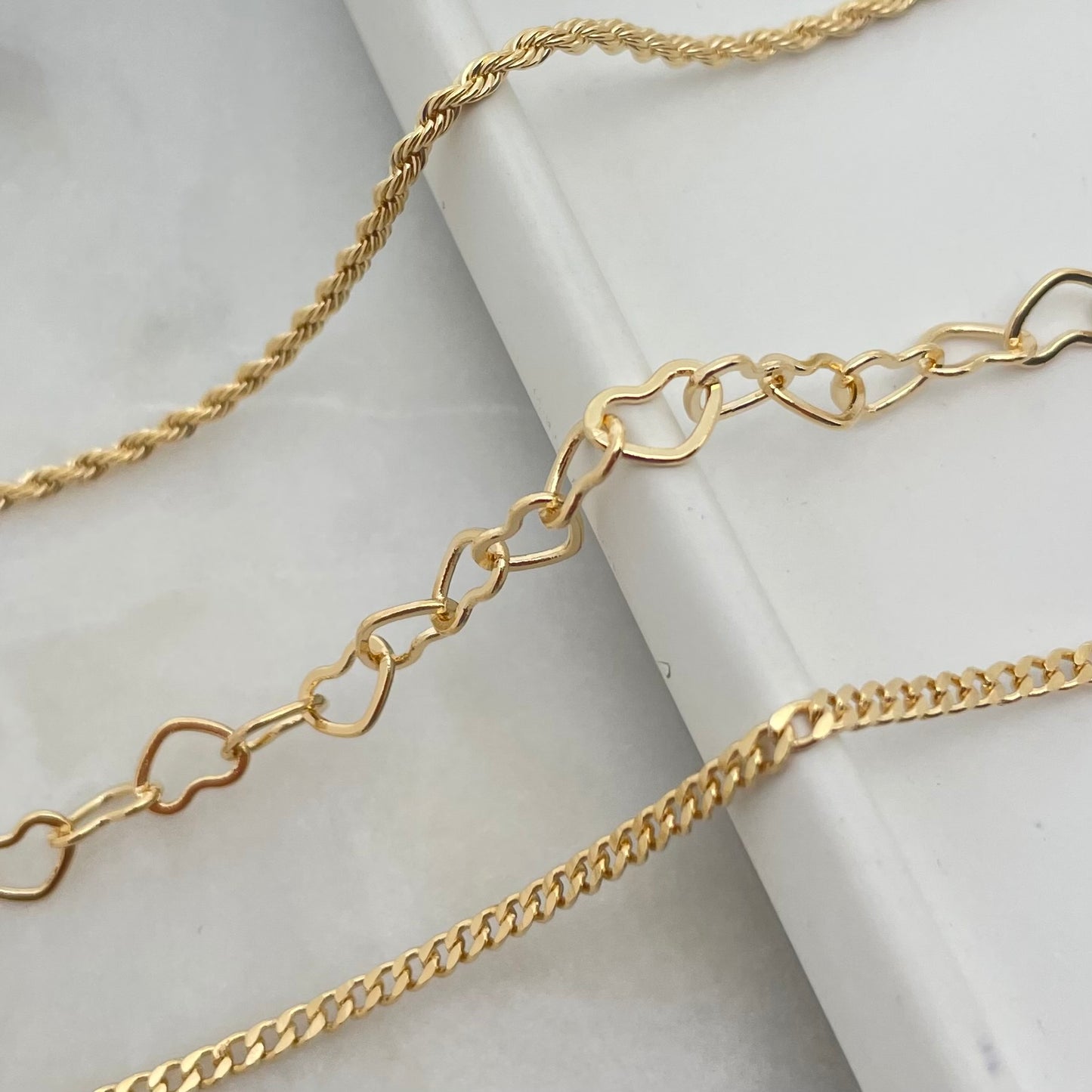 Details of anklet chain anklets in gold over white layout.