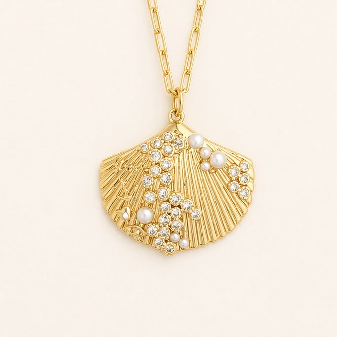 Gold necklace with a shell pendant featuring pearls and crystals on a light beige background