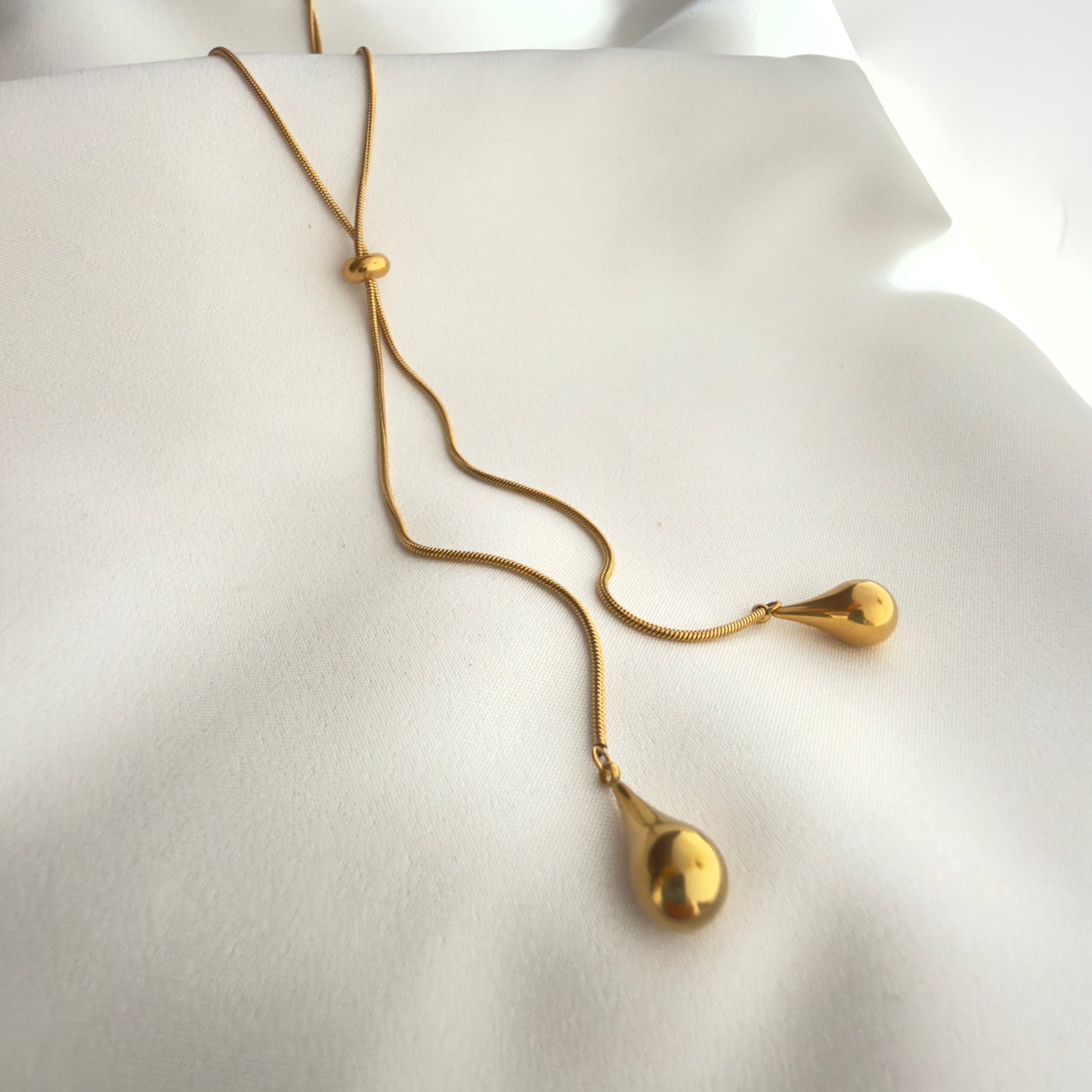 Gold necklace with teardrop pendants on a white silky fabric 