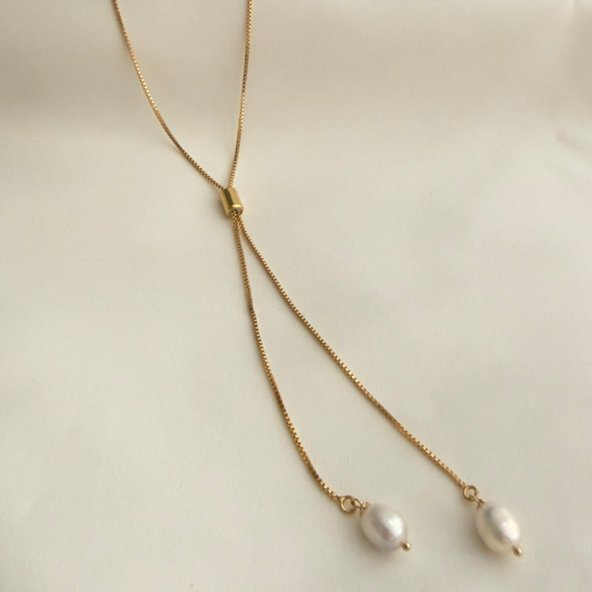 Gold necklace with pearl drops on a white satin background