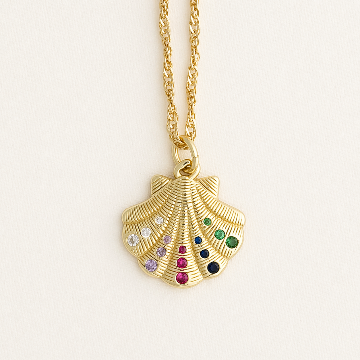 Gold shell pendant necklace with colorful gemstones on a light beige background