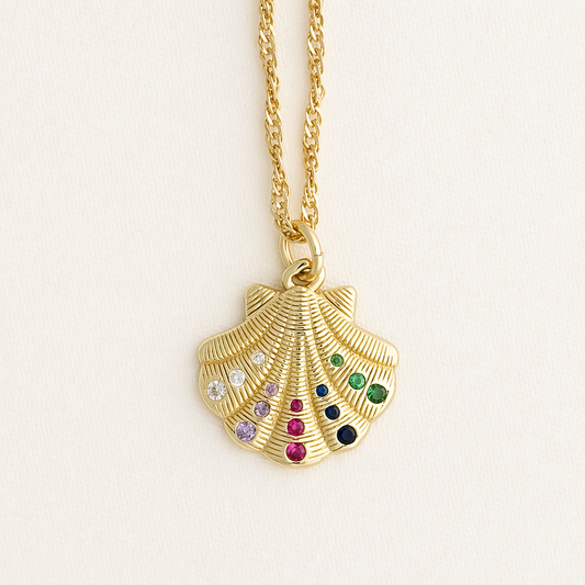 Gold shell pendant necklace with colorful gemstones on a light beige background