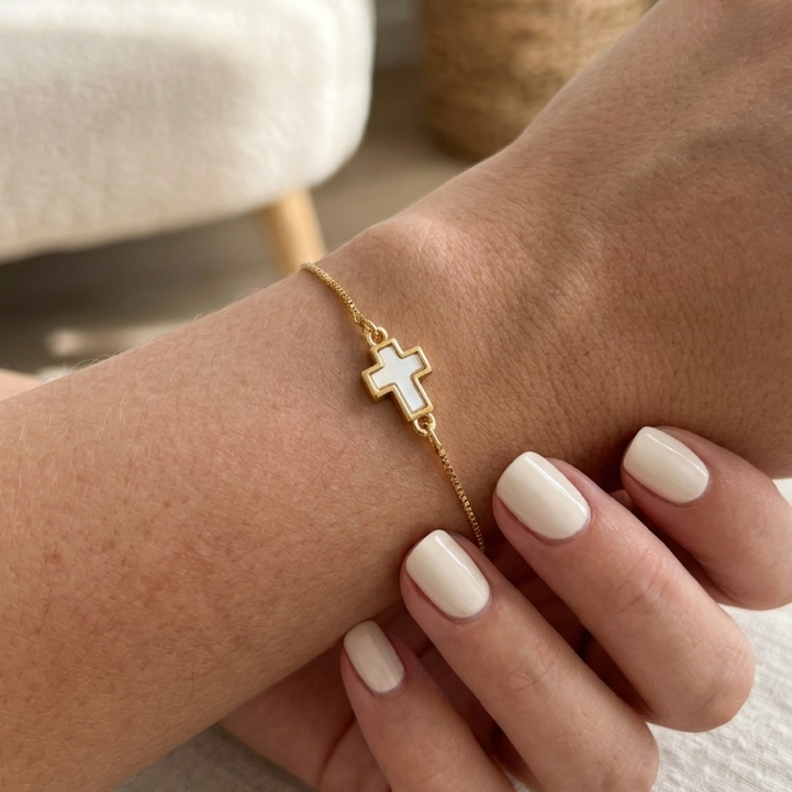 Gold plated bracelet with a cross charm on a wrist against a neutral background
