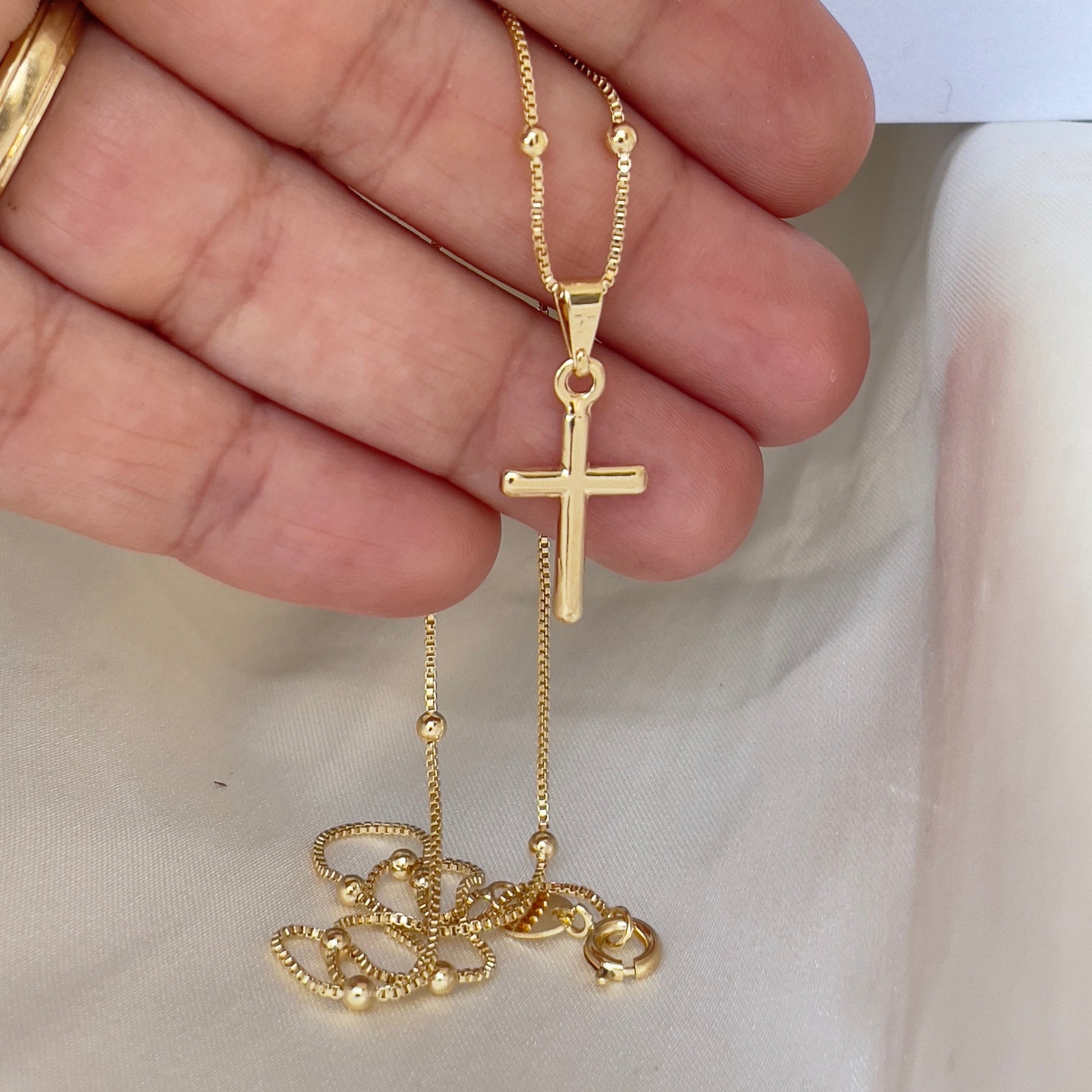 Cross Necklace, plain cross pendant. Materials: 18k gold filled over white brass, shown in hand and white silk background