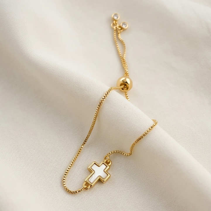Gold plated bracelet with a mother of pearl cross charm on a soft beige background