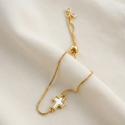 Gold plated bracelet with a mother of pearl cross charm on a soft beige background