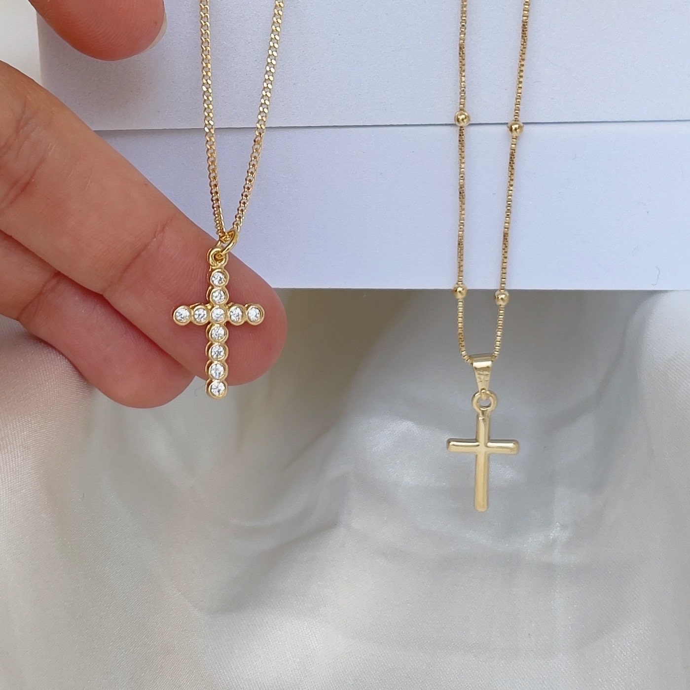Cross Necklace, plain cross pendant and cubic zirconia cross pendant. Materials: 18k gold filled and cz, shown in hand and white silk background