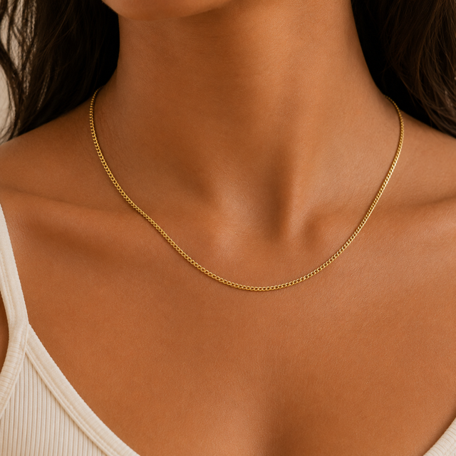 Gold curb chain necklace on a person's neck with a neutral background