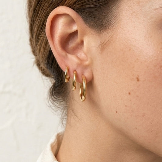Close-up of a person wearing gold hoop earrings with a neutral background