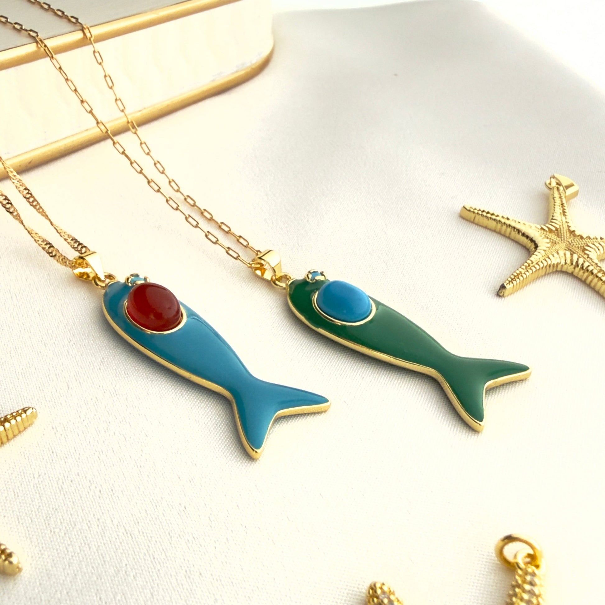 Two fish-shaped necklaces on a white surface with gold chains.