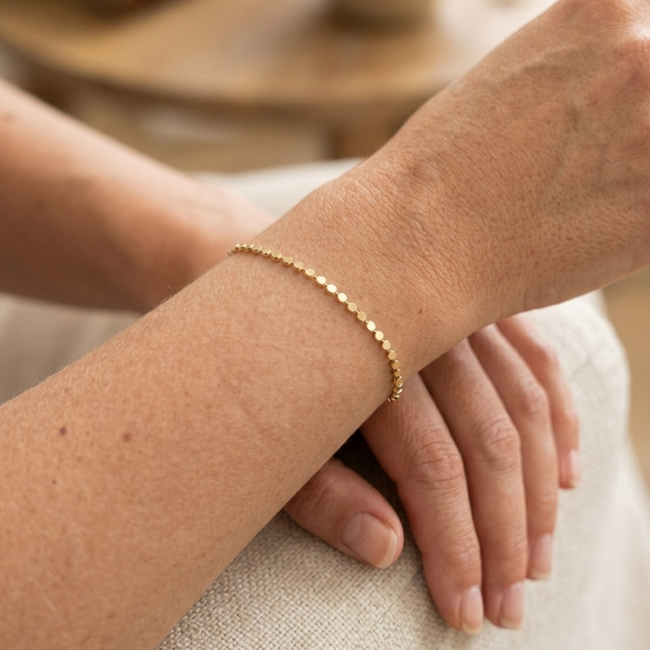 Close-up of a wrist wearing a gold flat disc bracelet with a blurred background