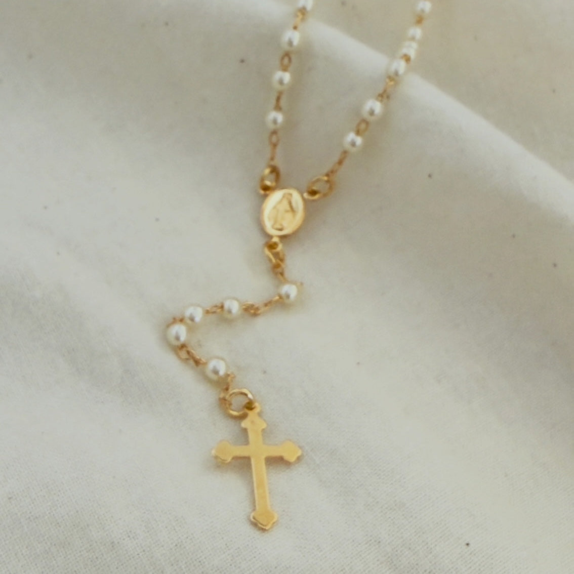 Gold filled rosary necklace with a cross pendant on a beige fabric background