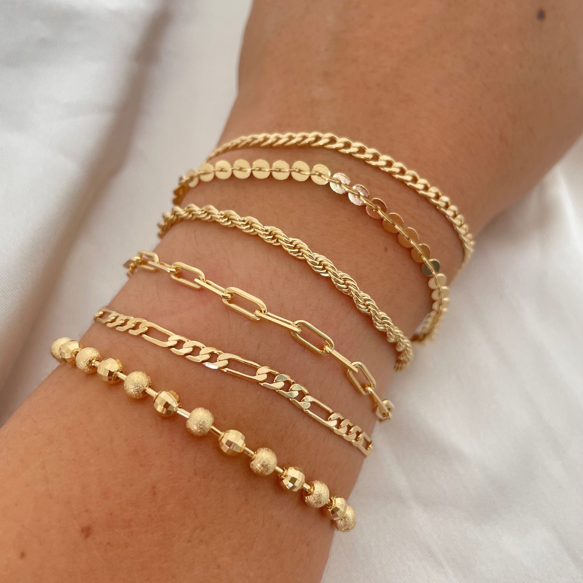 Multiple gold bracelets for everyday jewelry and stacking. Paperclip, cuban link, rope chain, coin disc bracelet, beaded bracelet, figaro chain 
