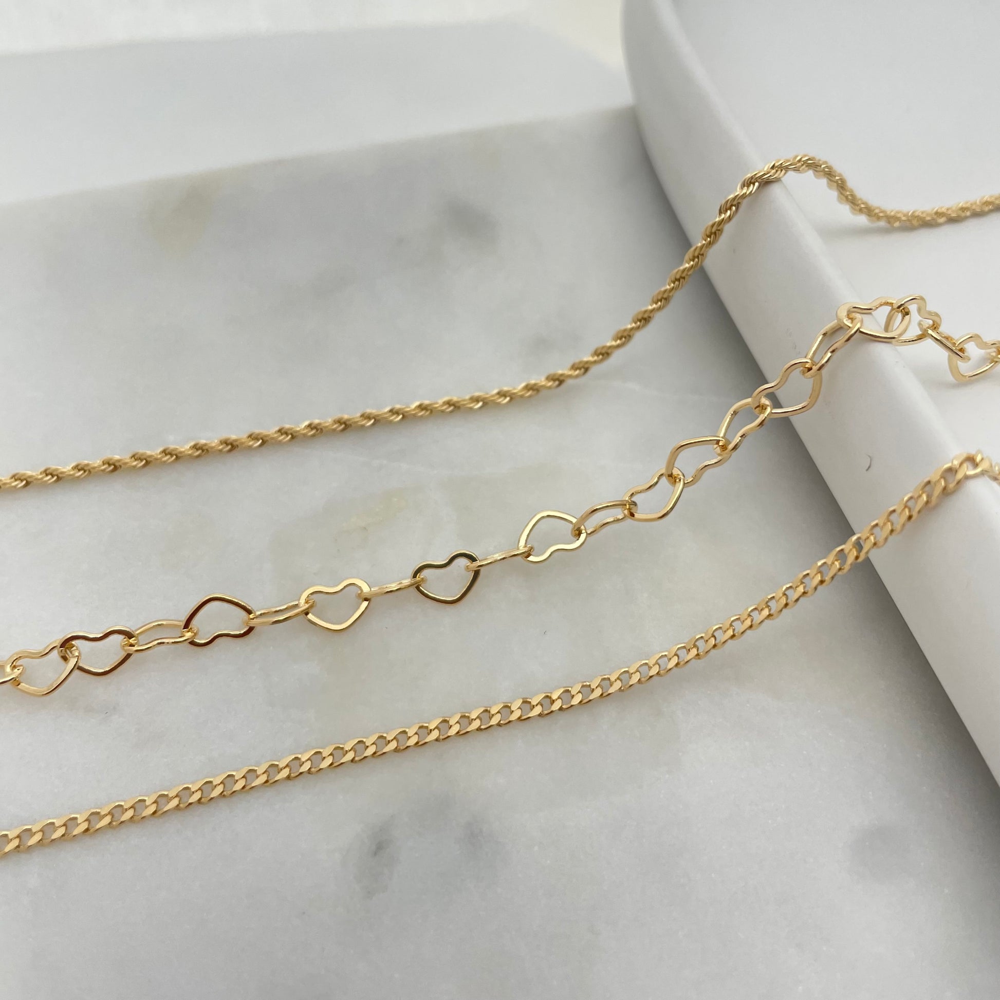 Rope, heart link and curb chain anklets display over white background 
