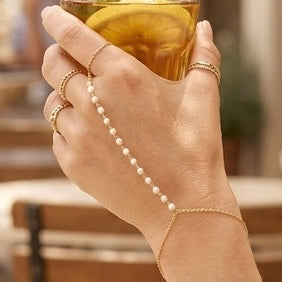 Hand wearing a gold filled pearl hand chain bracelet holding a glass of beer.