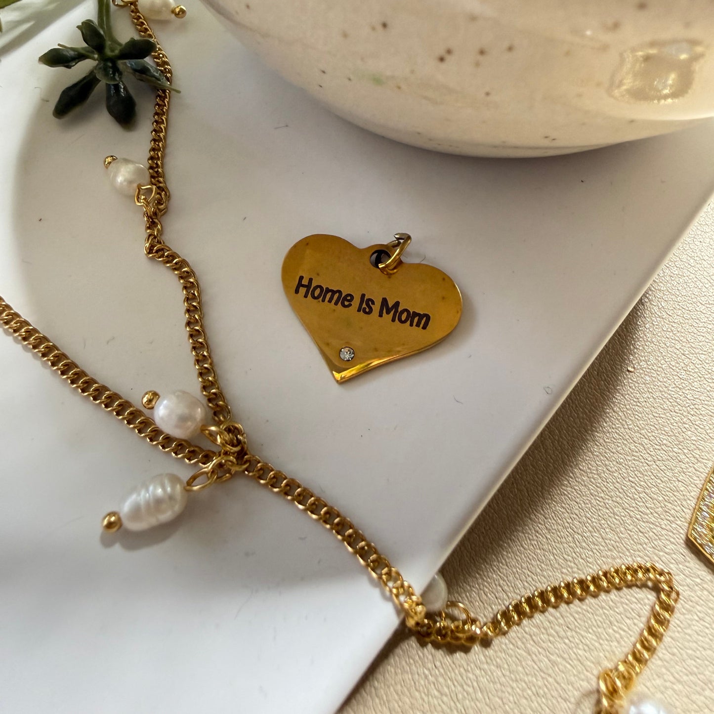 Gold necklace with heart-shaped 'Home is Mom' tag on a white dish