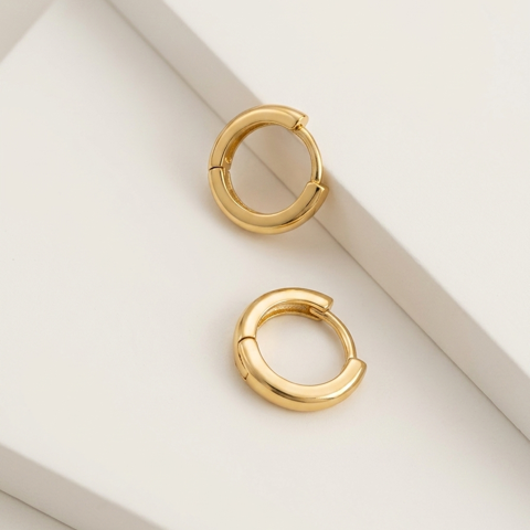 A pair of gold-toned split hoop earrings displayed on a clean, minimalist white geometric surface.