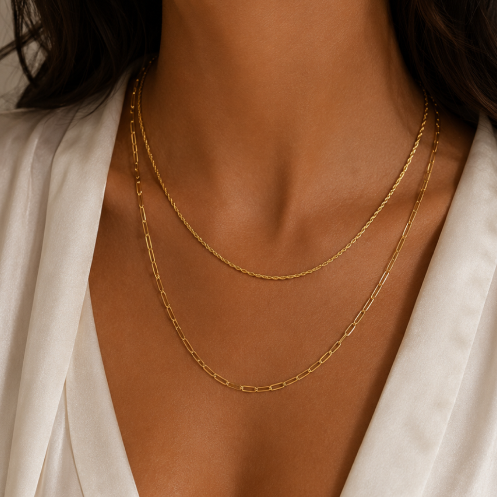 Close-up of a person wearing 2 gold chain layered necklaces with a white satin garment.