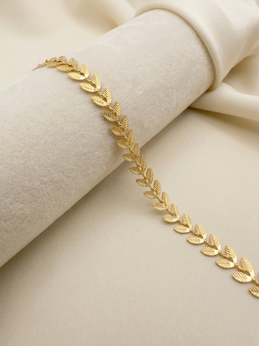 A delicate gold filled leaf chain bracelet draped elegantly across a soft, cream-colored fabric and velvet roll.