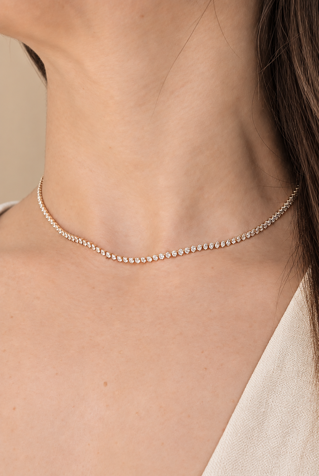 A delicate gold tennis necklace with small clear stones worn on a model's neck.