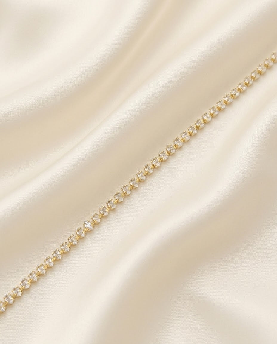 A delicate gold tennis marquise choker with czstones, laid diagonally across draped cream-colored satin fabric