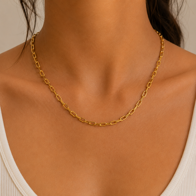 Gold paperclip chain necklace on a person with a neutral background